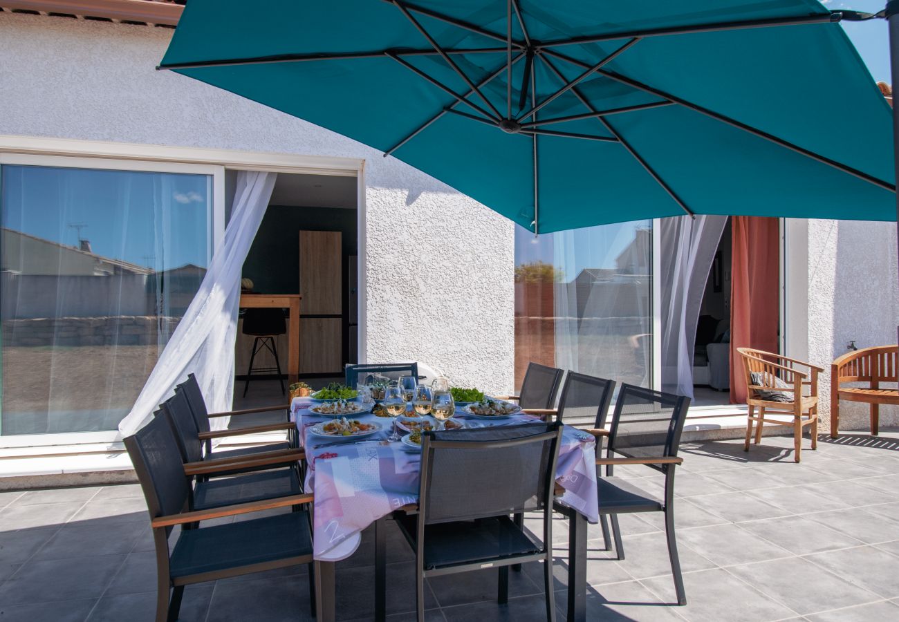 Großer Außentisch gedeckt auf der Terrasse, unter blauem Sonnenschirm.