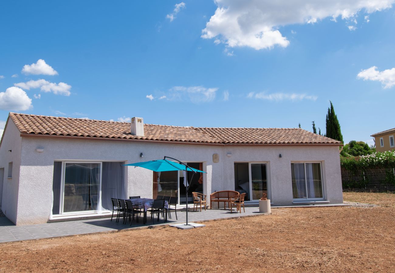 Fachada de casa vacacional con terraza equipada y sombrilla.